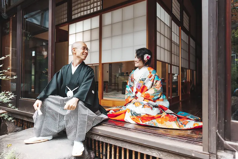 film-marie07 Jolie万梨恵の着付けとヘアメイクで和装ロケーション前撮り、古民家の縁側で談笑する色打掛の新婦と紋付袴の新郎を撮影しました。